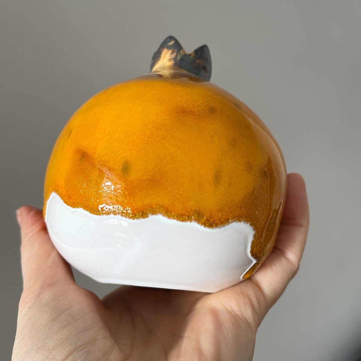 Handmade ceramic pomegranate with glossy yellow glaze and white base, decorative pottery fruit in hand