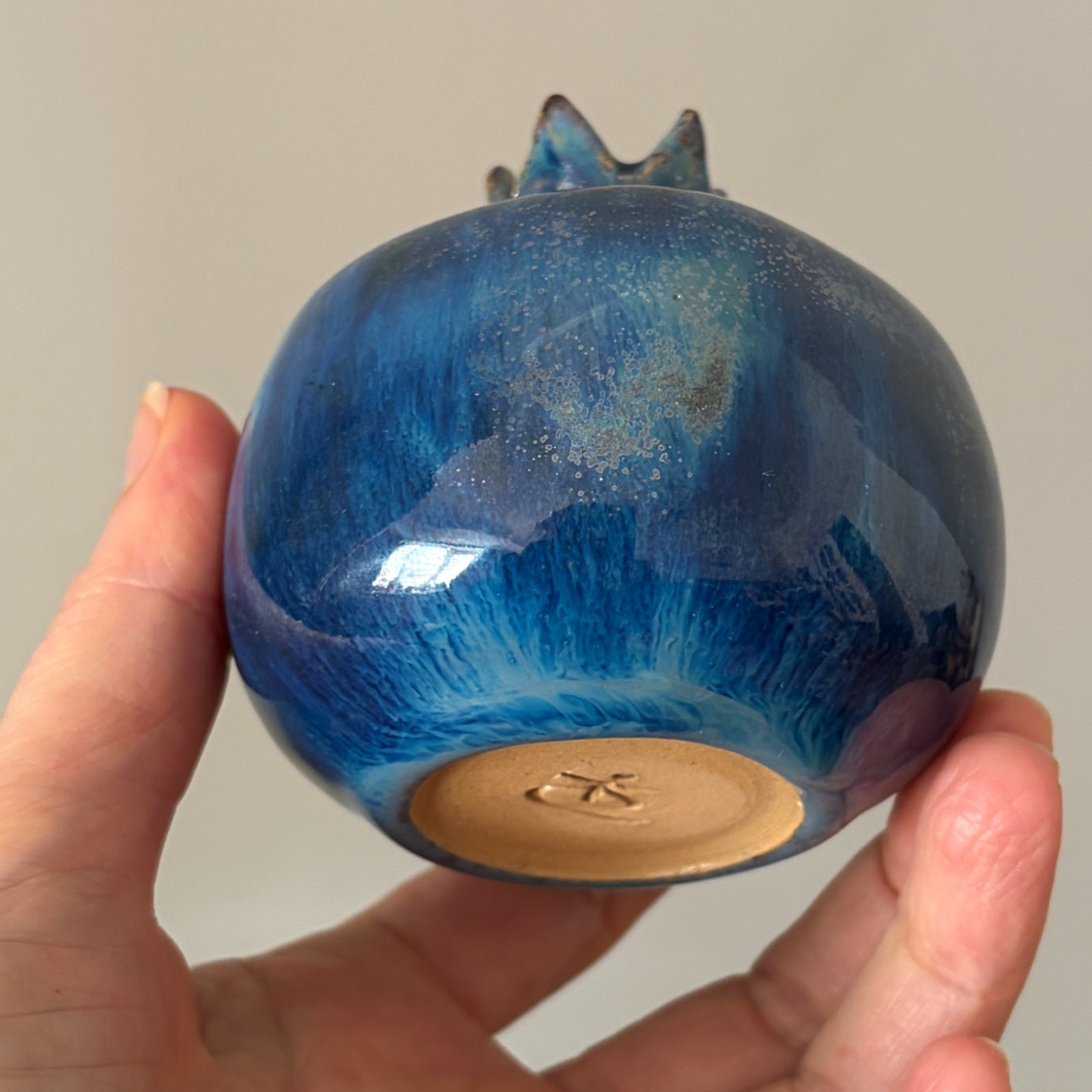 Handcrafted ceramic pomegranate held in hand showing its glossy blue surface
