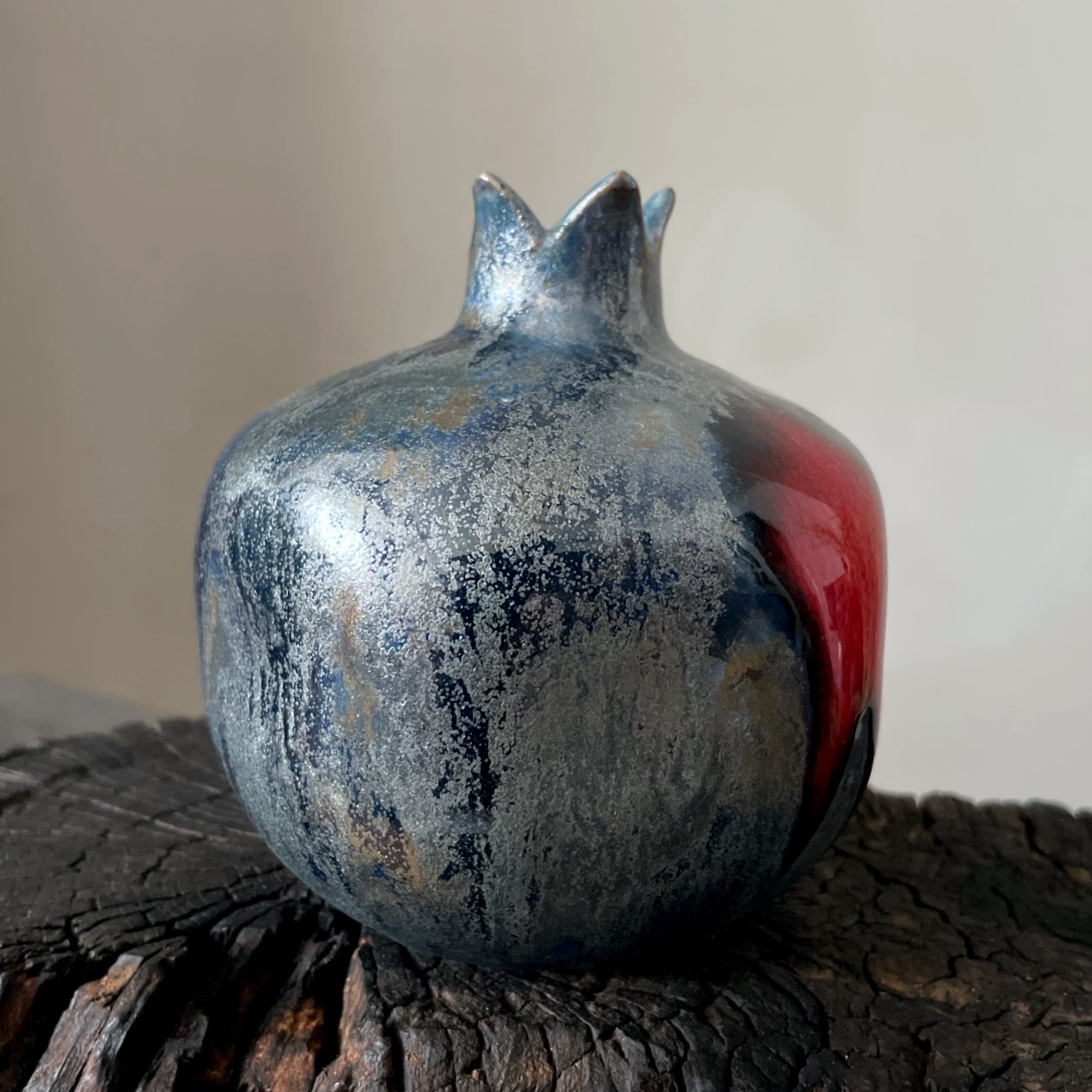 Handcrafted ceramic pomegranate with red accent and dark textured glaze
