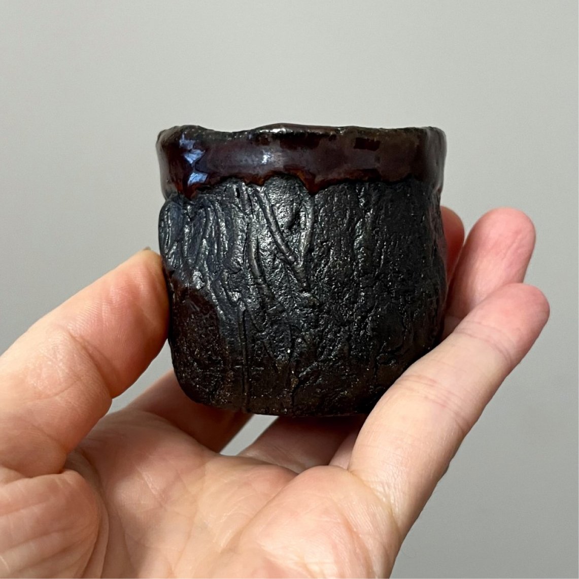 Small black ceramic yunomi cup held in hand