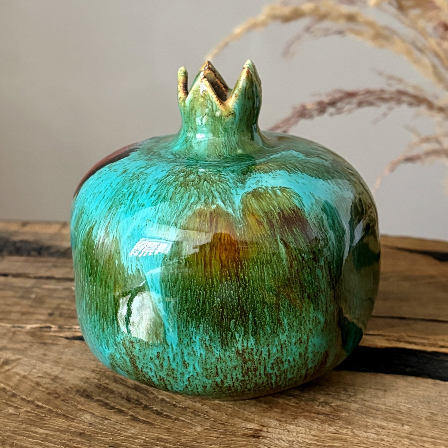 Side view of glazed ceramic pomegranate ornament with rich green and blue tones