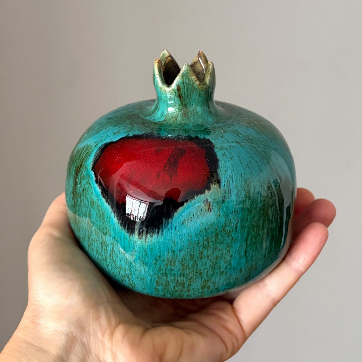 Small ceramic pomegranate held in hand showing its glossy glazed surface
