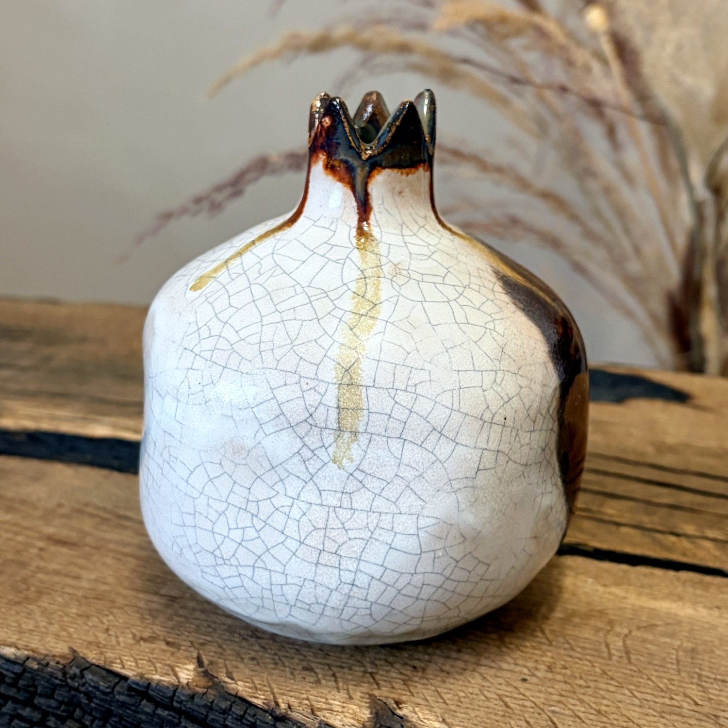 White glazed ceramic pomegranate ornament with dark sculpted crown