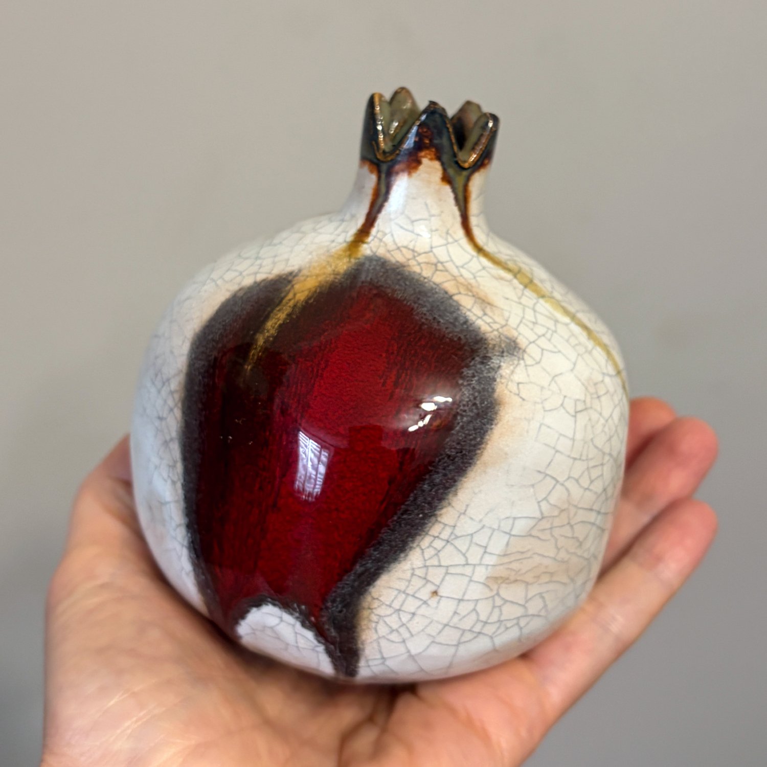 Handcrafted pottery pomegranate held in hand with white crackle finish