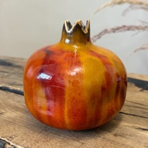 Close-up of ceramic pomegranate with vibrant orange and red glazed surface