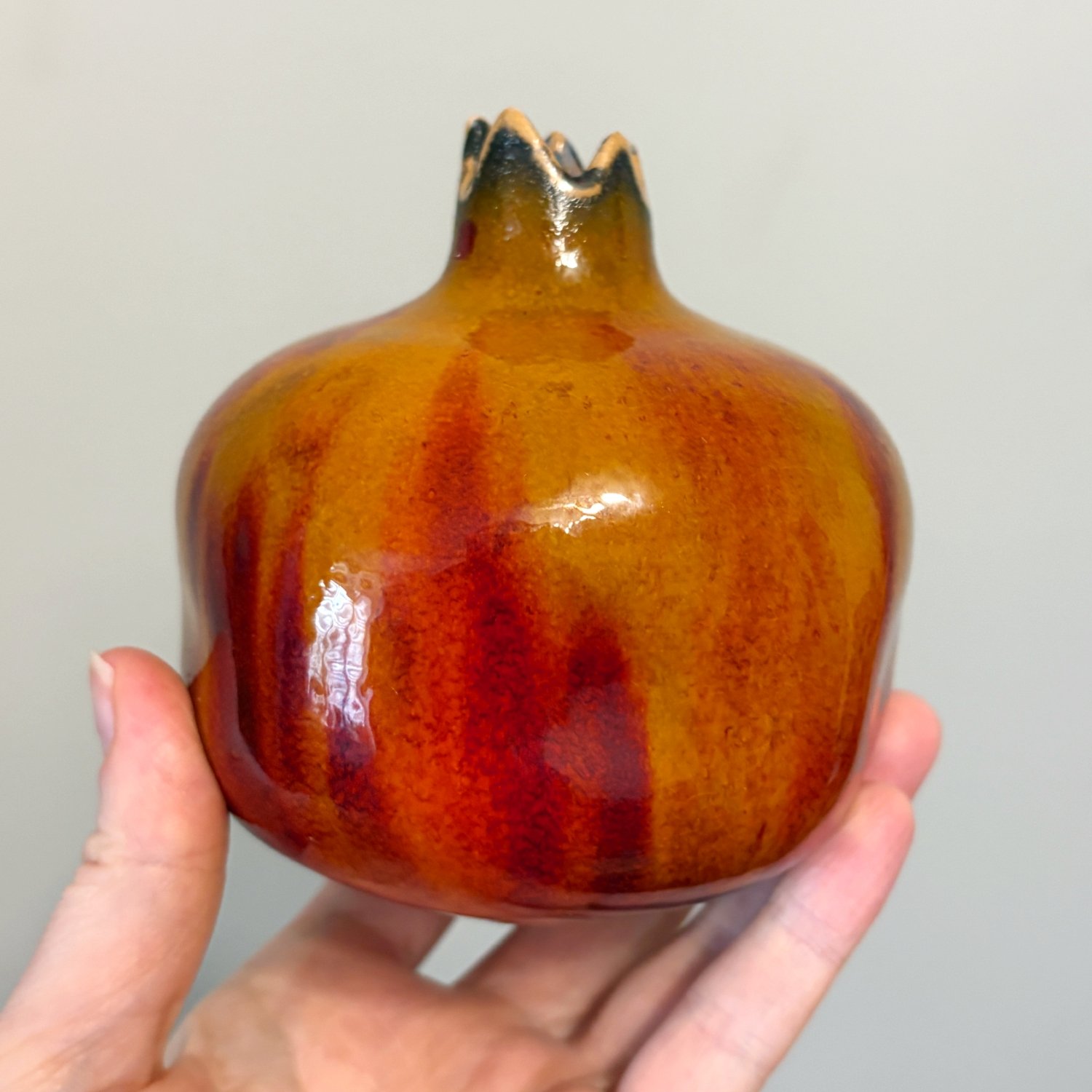 Ceramic pomegranate held in hand showing its rounded shape and glossy finish