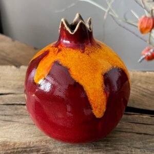 Handmade ceramic pomegranate vase with red and yellow glaze on wooden table